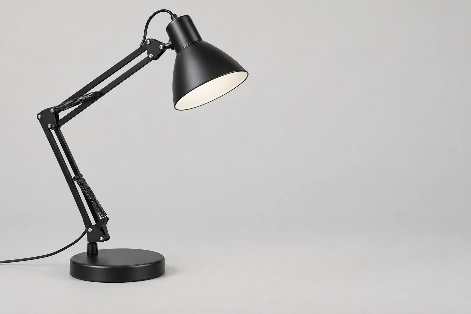 Black swing-arm desk lamp with a round base and cone shade, without annotations